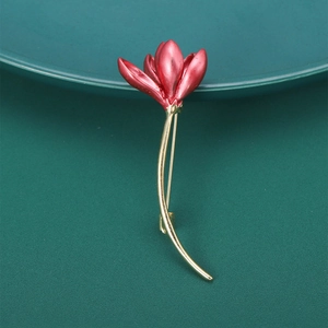 Elegant red enamel magnolia flower brooch with golden stem on deep green background