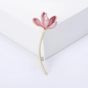 Close-up of pink enamel magnolia brooch with gold stem on a white geometric stand