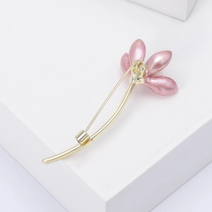 Macro detail of enamel magnolia flower brooch with pink petals and gold-plated safety pin