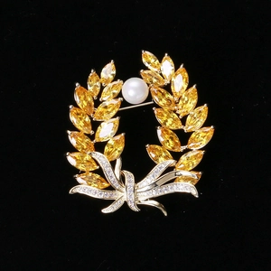 Close-up of wheat brooch with golden zircons and a white pearl on black background