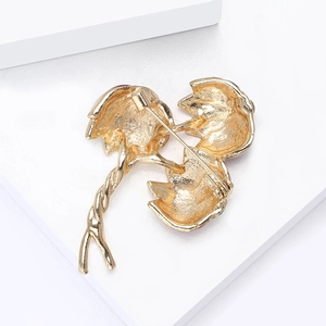 Macro detail of golden flower brooch back showing safety pin clasp and matte metal texture