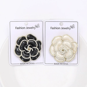 Détail de broches camélia en émail avec bordure perlée en noir et crème sur carte