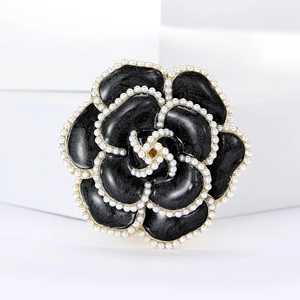 Détail de la broche camélia en émail noir avec perles blanches et bordure dorée élégante