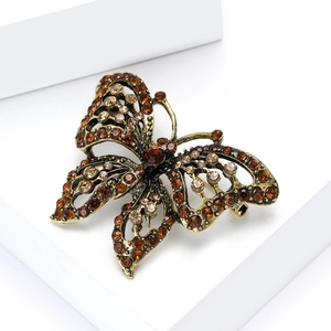 Macro shot of gold butterfly brooch with amber rhinestones on white platform