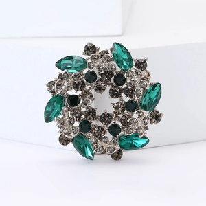 Vintage alloy floral brooch with emerald green crystals and grey diamonds on white pedestal