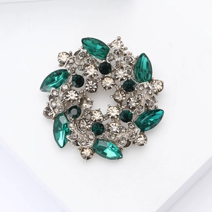 Detailed top view of retro wreath brooch with emerald glass and silver plating