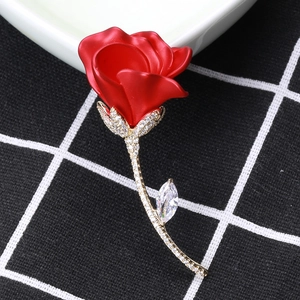 Détail d'une broche rose rouge avec tige dorée et accent de feuille en zircon brillant