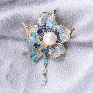 Luxurious flower brooch with blue zircon petals and large pearl on silk background