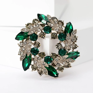 Macro detail of luxury baroque crystal wreath brooch with green emerald gems and silver leaves