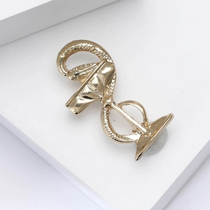 Close-up of golden medical Caduceus brooch with snake design on a white geometric stand