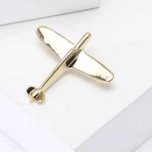 Minimalist polished gold airplane brooch pin for suits on a white geometric platform