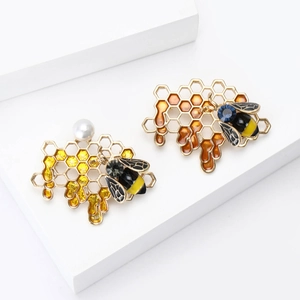 Enamel bee and honeycomb brooch set with pearls and rhinestones on a white stand