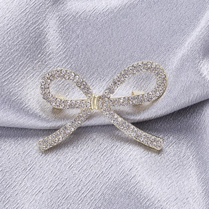 Detail einer eleganten goldenen Schleifenbrosche mit Strass auf grauem Seidenstoff