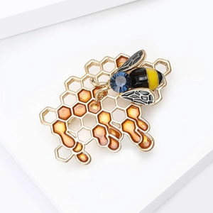 Enamel honeycomb bee brooch with blue gemstone and gold plating on white platform