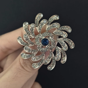 Détail d'une broche florale argentée avec cristaux clairs et pierre centrale bleu foncé
