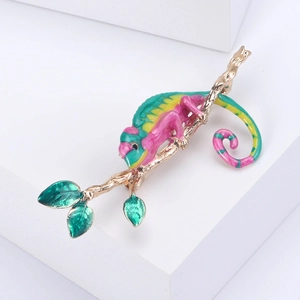 Détail d'une broche caméléon en émail coloré avec branche dorée sur fond blanc épuré
