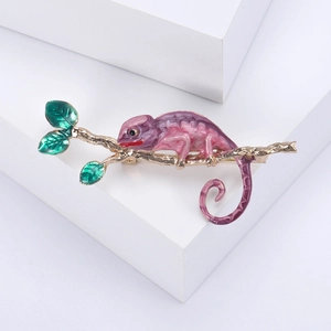 Vue détaillée d'une broche caméléon en émail rose sur une branche dorée aux feuilles vertes