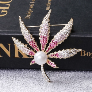 Makroaufnahme einer Ahornblatt-Brosche mit rosa Kristallen und Perle auf Buch