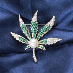 Details einer Blattbrosche mit grünen Kristallen und Perle auf Seidenhintergrund
