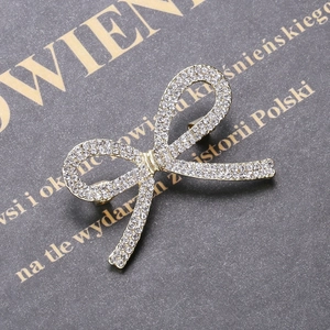 Detail einer goldenen Schleifenbrosche mit Strass auf grauem strukturiertem Hintergrund