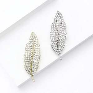 Elegant gold and silver leaf brooches with sparkling crystals on white geometric stands