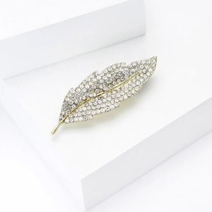 Close-up of gold-tone leaf brooch with sparkling clear crystals on white pedestal