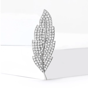 Elegant silver leaf brooch with sparkling crystals on minimalist white pedestals