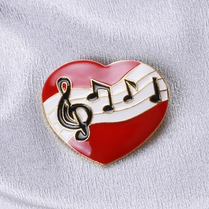 Macro d'une broche cœur en émail rouge avec notes de musique sur satin argenté