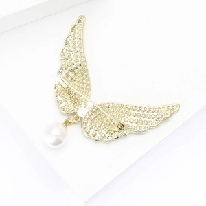 Détail d'une broche ailes d'ange dorées avec texture évidée et perle suspendue