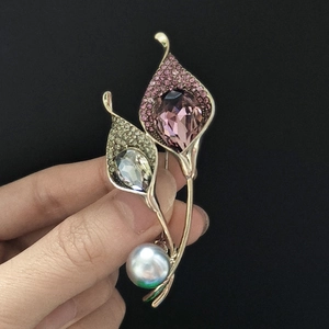 Detailed close-up of floral brooch with purple crystal drop and pearl on black background