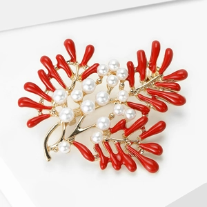 Detailed close-up of golden brooch with red coral enamel branches and elegant white pearls