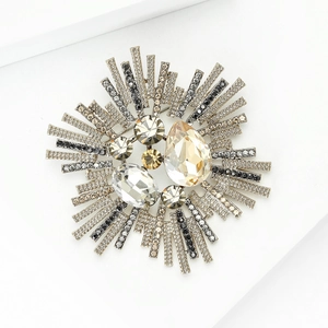 Détail d'une broche soleil dorée avec cristal champagne et strass noirs polis