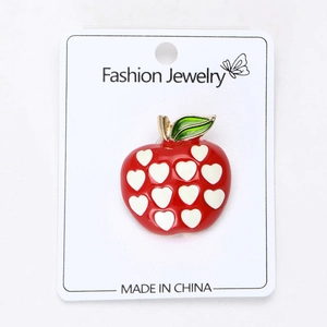 Detail of red apple alloy brooch with heart pattern on a jewelry display card