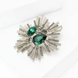 Détail d'une broche baroque argentée ornée de cristaux vert foncé et de pierres grises