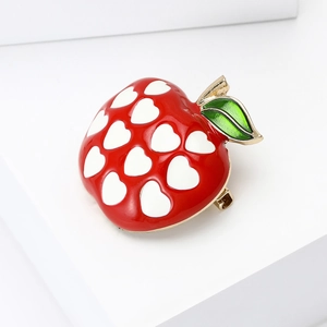 Detail of red enamel apple brooch with white heart patterns and green leaf texture