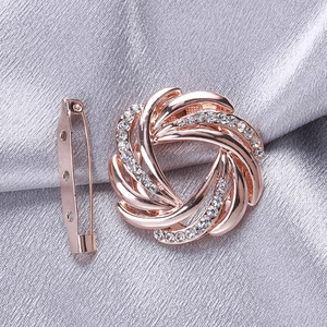 Elegant rose gold swirling flower brooch with sparkling rhinestones on silk background