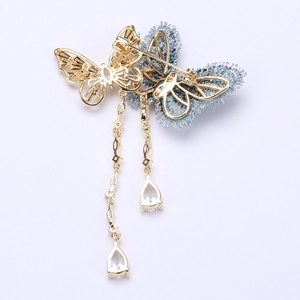 Détail d'une broche papillon en tissu brodé avec pompons dorés et cristaux en forme de poire