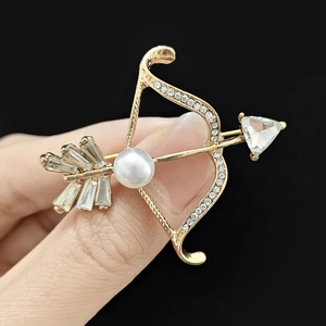Détail de la broche en forme d'arc et de flèche avec strass et une perle blanche centrale