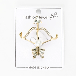Détail d'une broche arc et flèche dorée avec des strass et une perle blanche centrale