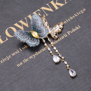 Détail de broche papillon brodée bleue avec pompons dorés et cristaux sur fond texturé