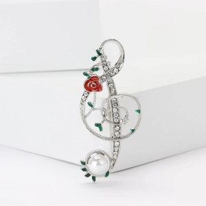 Détail macro d'une broche clé de sol avec rose rouge, strass blancs et perle
