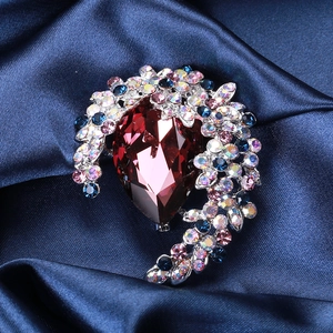 Detail of luxury crystal brooch with pear-shaped red stone on blue satin background