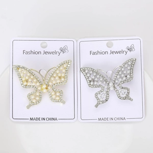 Détail de broches papillon avec perles blanches et strass en finitions or et argent