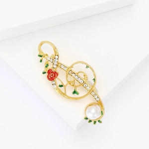 Broche note de musique dorée avec rose rouge et perle sur un support blanc épuré