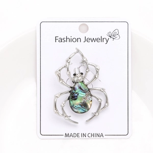 Macro shot of spider brooch with abalone shell inlay and small rhinestones on white card