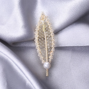 Elegant gold leaf brooch with pearls and rhinestones on grey silk background