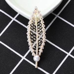 Elegant gold leaf brooch with pearls and crystals on a minimalist checkered fabric background