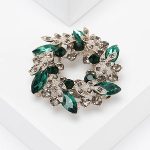 Close-up of emerald green marquise crystals and silver leaf textures on a floral brooch