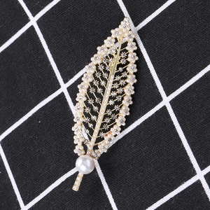 Detailed view of leaf brooch with white pearls and sparkling rhinestones on gold metal