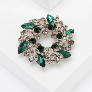 Macro detail of alloy flower brooch with deep green rhinestones and silver leaf accents